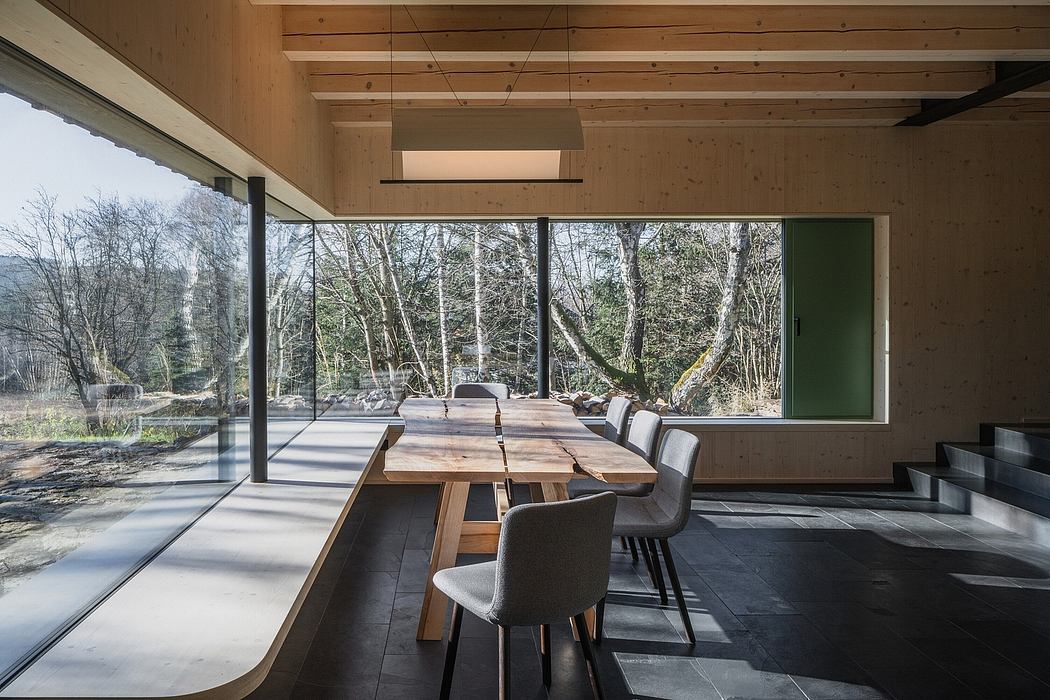 A modern minimalist dining area with a large wooden table, plush chairs, and expansive windows showcasing a lush forest view.