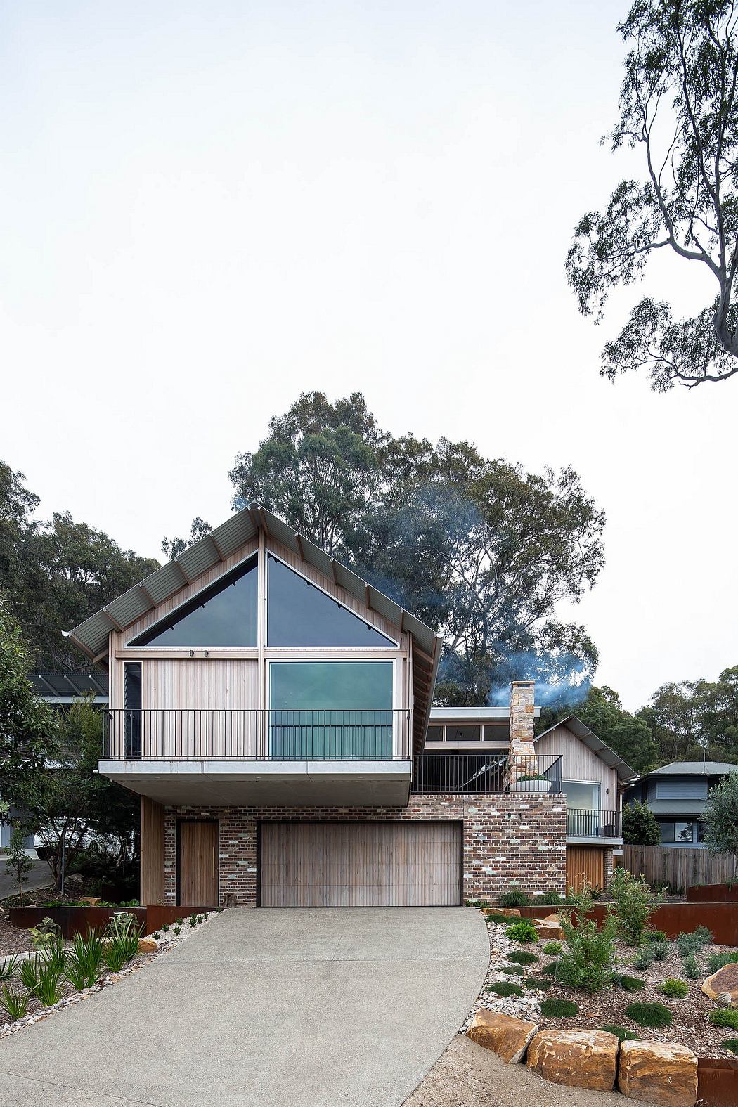 Contemporary two-story home with wood, glass, and brick facade surrounded by lush greenery.