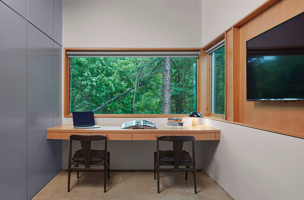 A modern home office with a large window overlooking a lush forest landscape.
