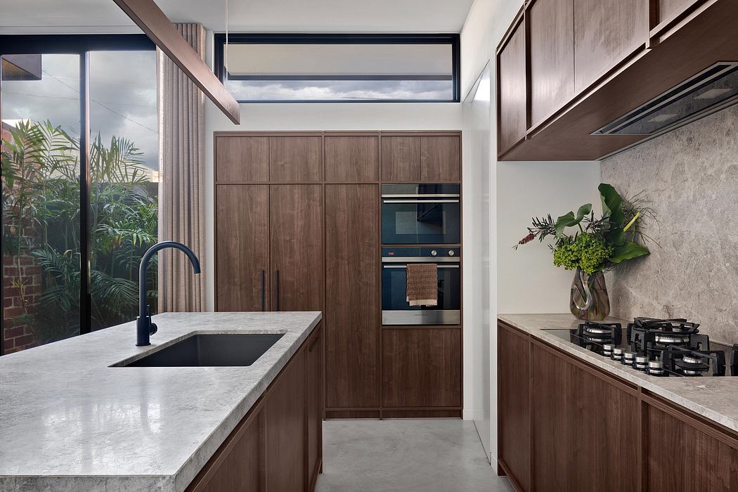 A modern kitchen with sleek wooden cabinetry, a marble countertop, and large windows providing natural light.