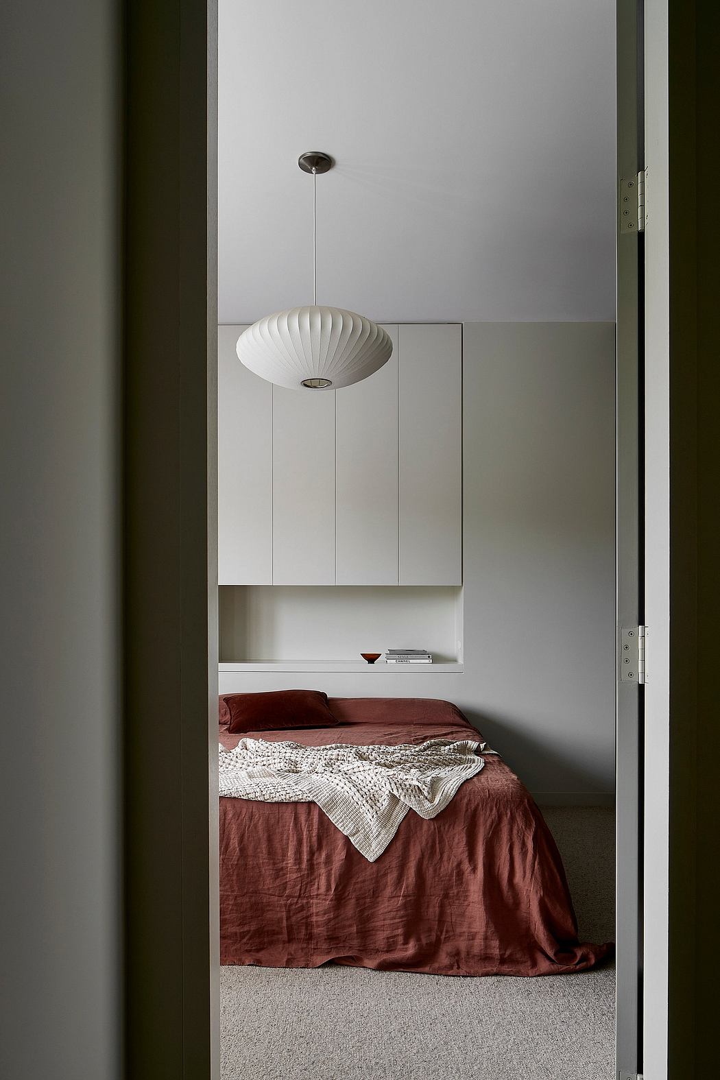 Minimalist bedroom with a spherical light fixture, built-in cabinetry, and red bedding.