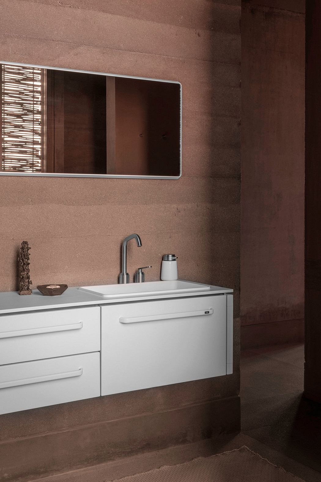 White minimalist vanity with chrome fixtures against a textured brown wall and a rectangular mirror.