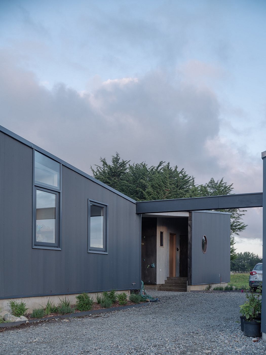 A modern, gray corrugated metal home with a prominent entryway and lush greenery.