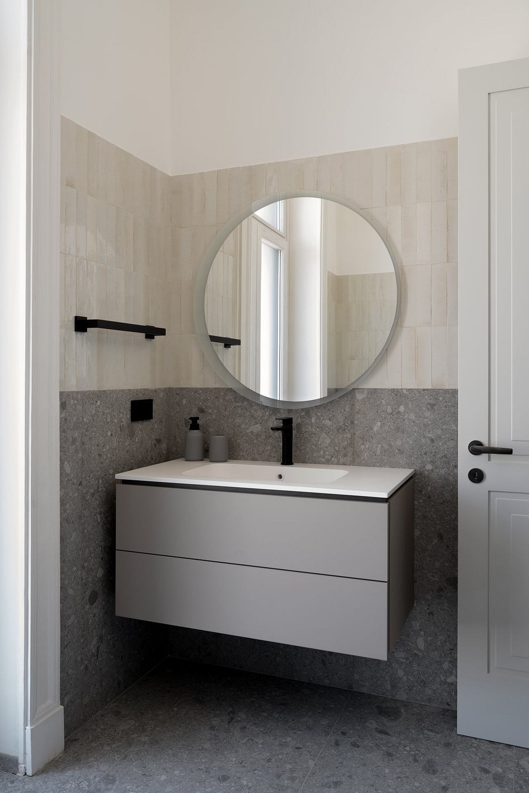 Minimalist bathroom with a circular mirror, floating vanity, and gray tile walls.