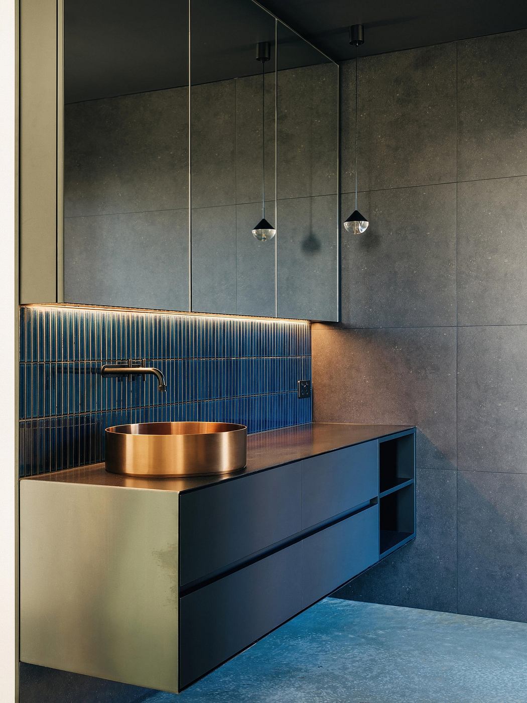A modern, minimalist bathroom design with a gold-toned sink, blue cabinets, and pendant lights.