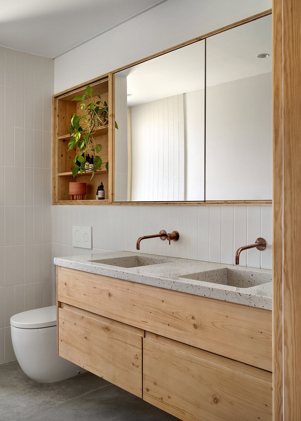 A minimalist bathroom with a wooden vanity, concrete counter, and shelving unit with a potted plant.