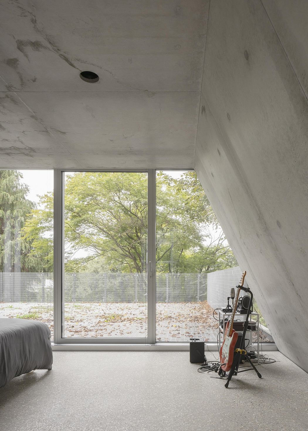 Minimalist interior with floor-to-ceiling windows, concrete walls, and a music setup in the corner.