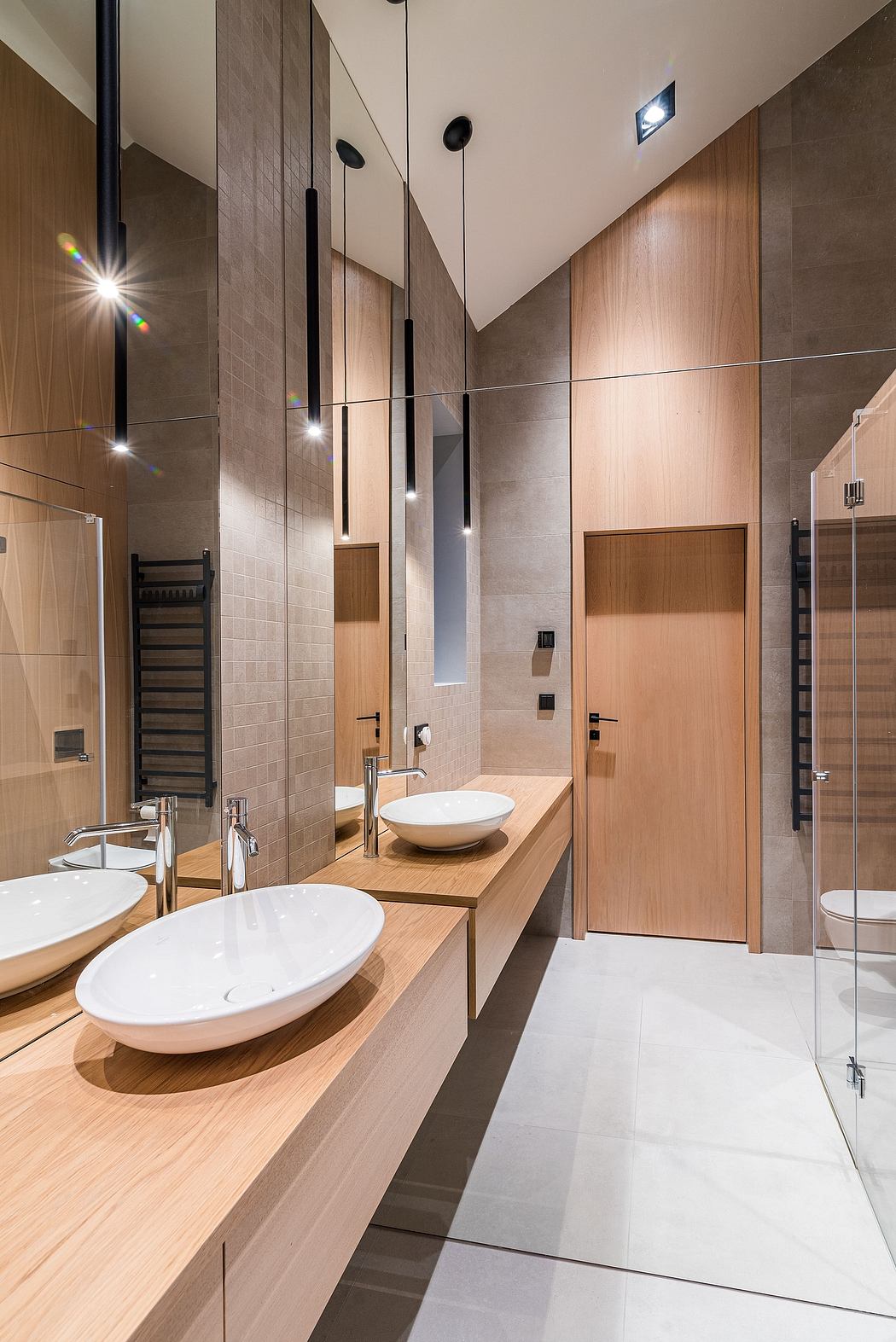 A modern, minimalist bathroom with sleek wood and tile surfaces, recessed lighting, and a floating vanity.