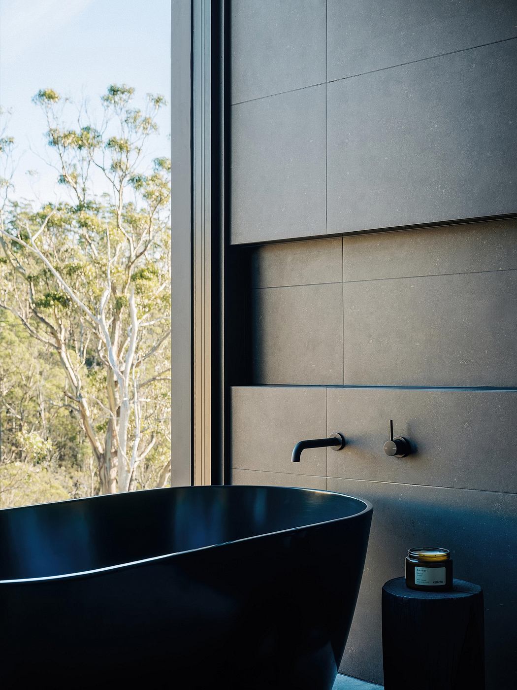 Sleek, modern bathroom with black bathtub, wall-mounted faucet, and lush outdoor view.
