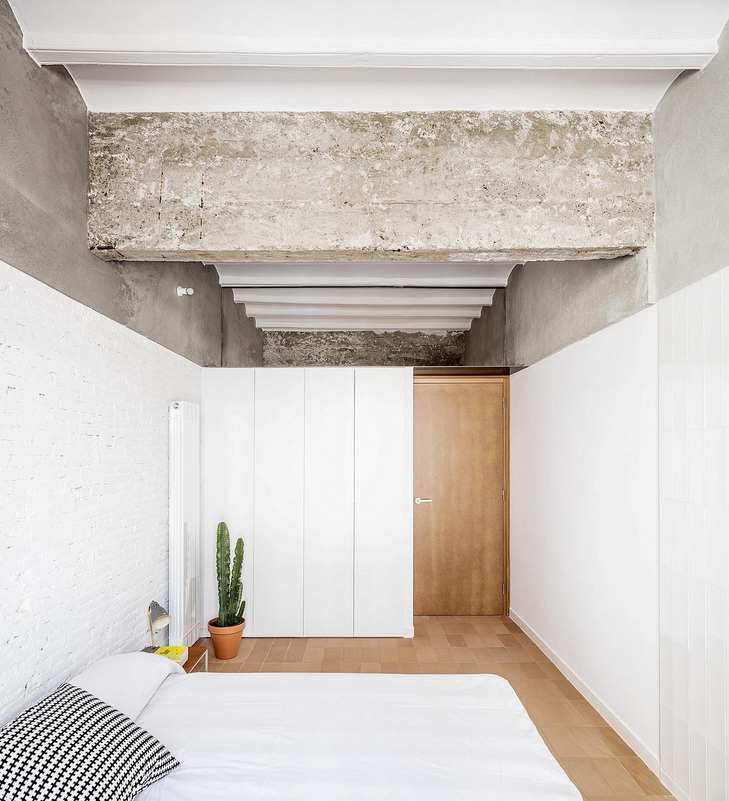 A minimalist bedroom with a concrete ceiling beam, wooden door, and a potted cactus.