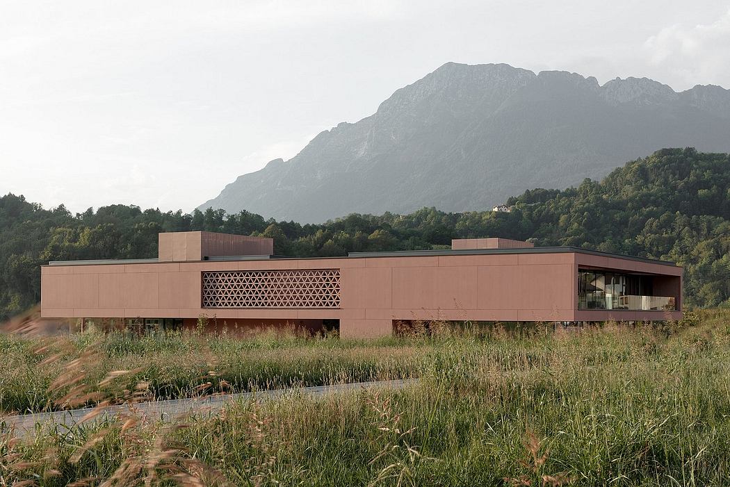 A modern, low-lying building with a perforated facade overlooking a mountainous landscape.