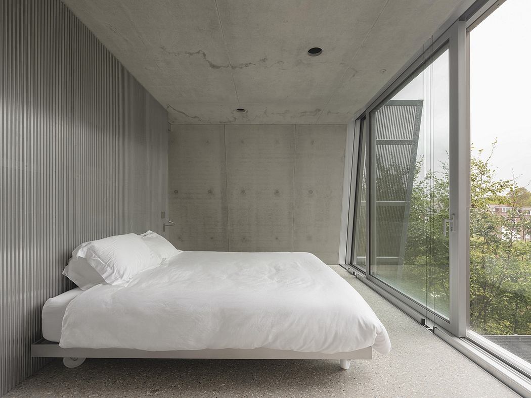 A minimalist concrete bedroom with floor-to-ceiling windows overlooking greenery.