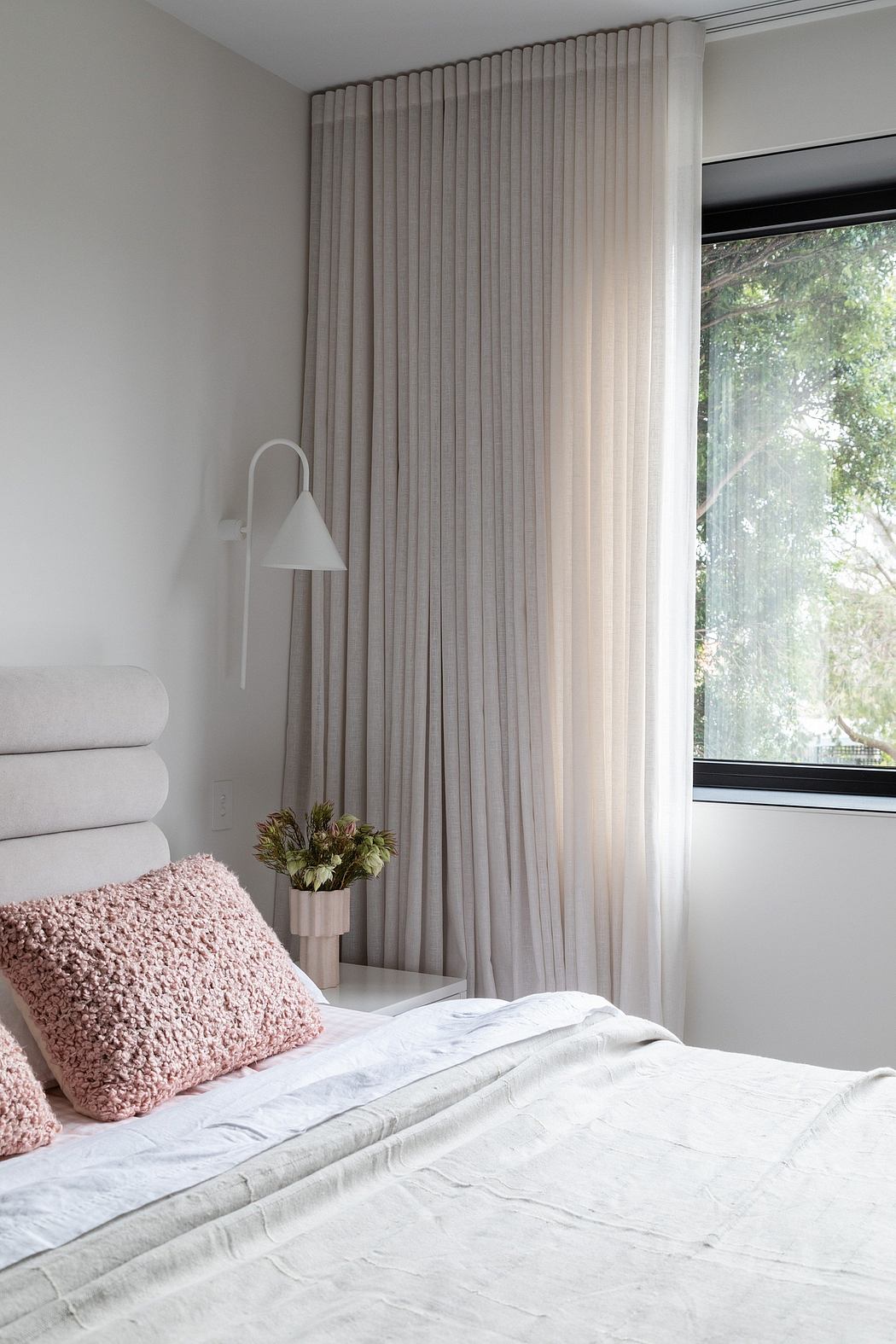 Neutral-toned bedroom with floor-to-ceiling curtains, accent pillow, and stylish sconce.