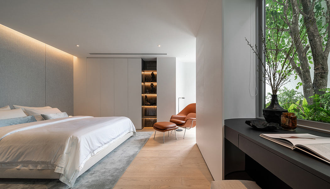 Minimalist bedroom with sleek built-in cabinetry, plush armchair, and expansive window overlooking lush greenery.