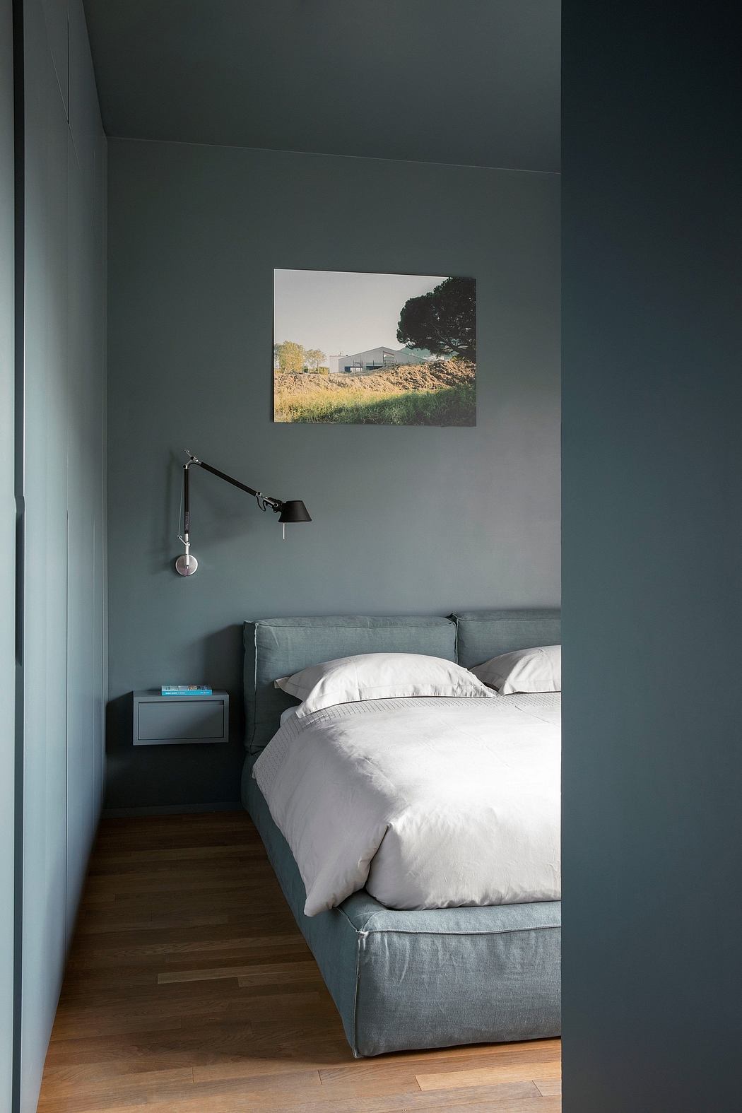 A cozy bedroom with a teal accent wall, hanging light, and a framed landscape artwork.