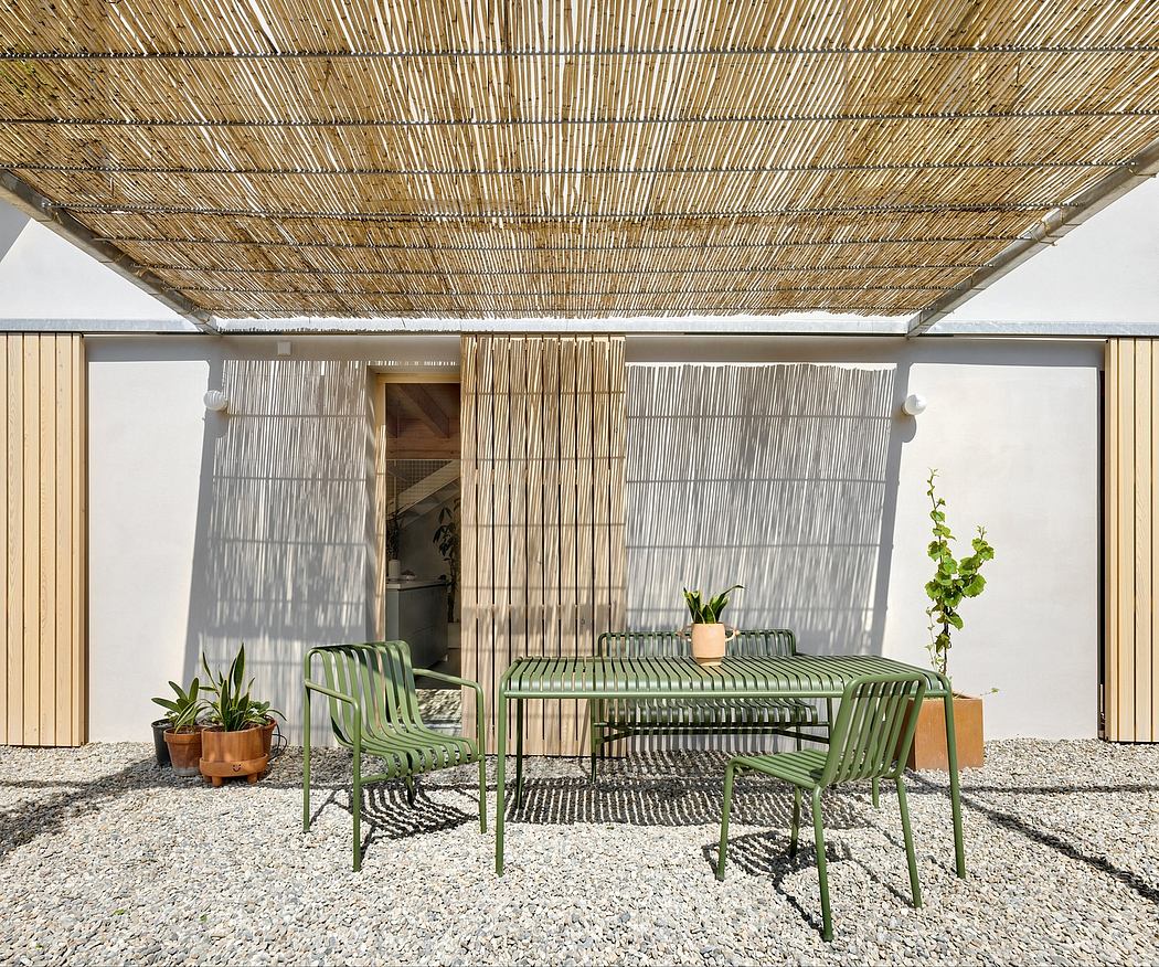 A modern outdoor patio space with a thatched roof, green metal furniture, and potted plants.