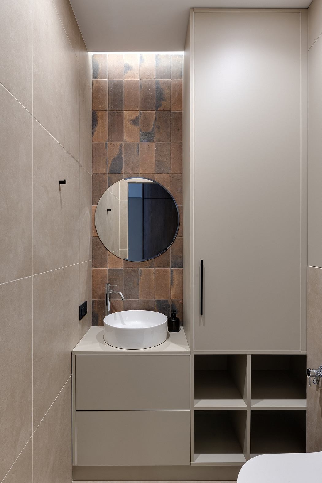 Modern minimalist bathroom with circular mirror, vessel sink, and tiled accent wall.