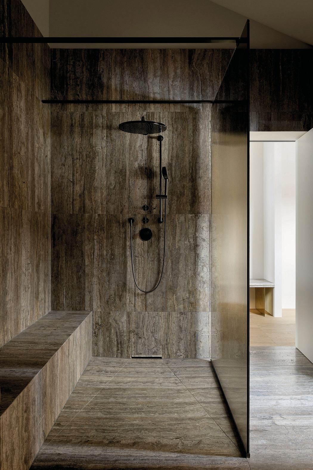 Rustic, minimalist bathroom design with stone-textured walls, black fixtures, and an overhead shower.