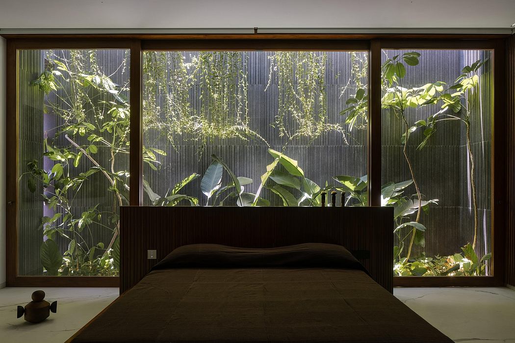 Lush, verdant indoor landscape visible through large windows frames a minimalist bedroom design.