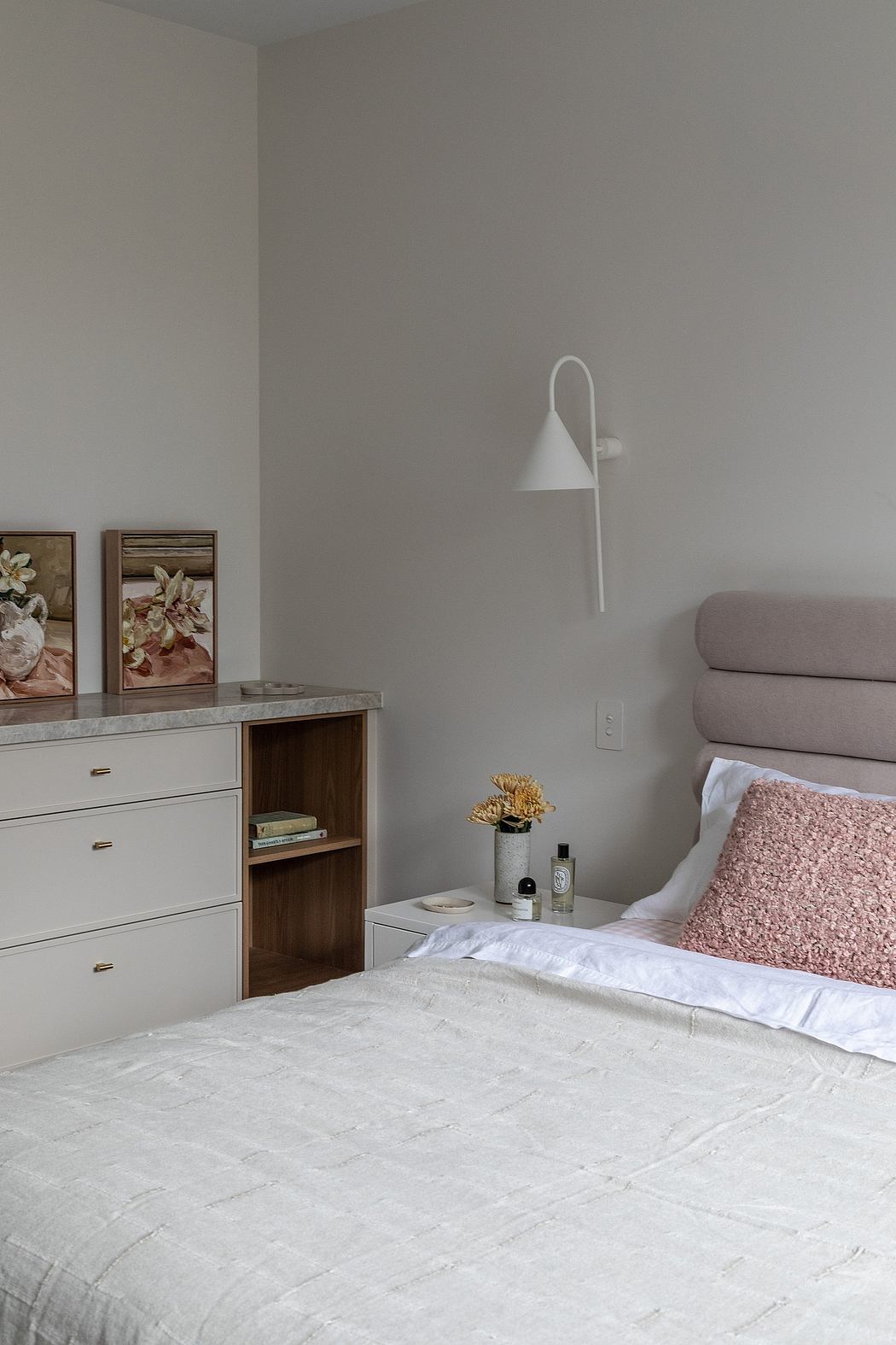 Minimalist bedroom with modern furnishings, wall sconce, and decorative artwork.