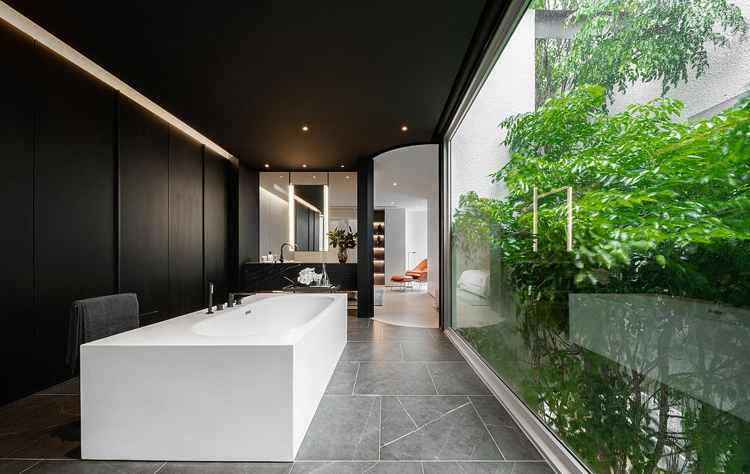Sleek, modern bathroom with monochrome tones, large white tub, and lush greenery outside.