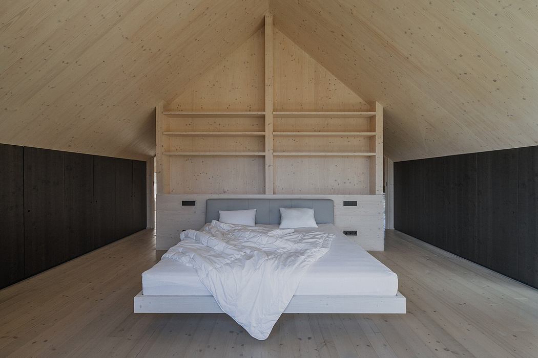 Spacious attic bedroom with wooden beams, minimalist design, and built-in shelving.