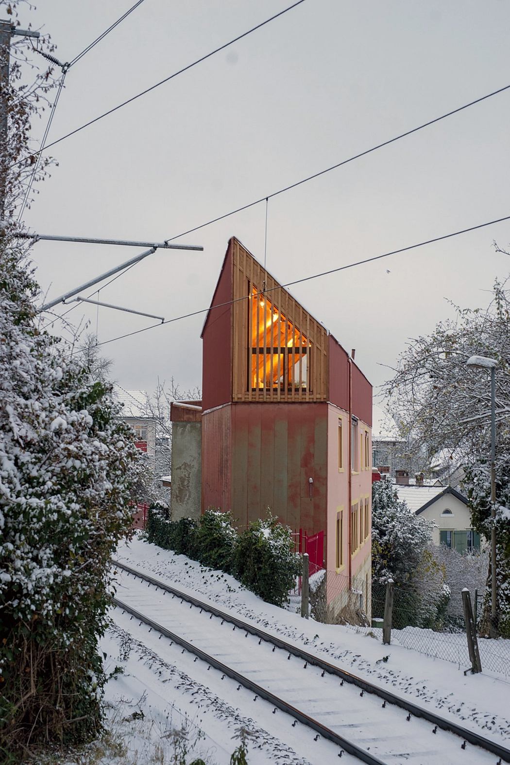 A snow-covered building with a unique angular roof design, appearing warm and cozy within.