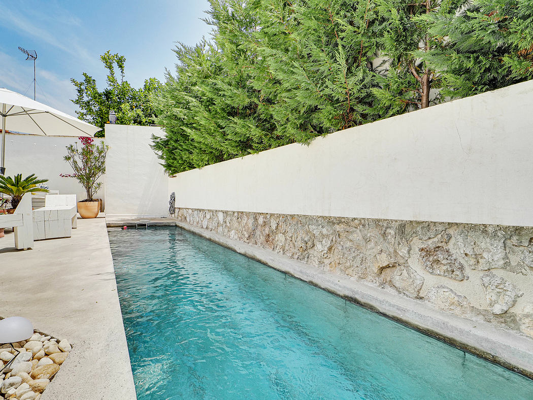 A serene backyard oasis with a refreshing pool, surrounded by lush greenery and a stone-walled patio.