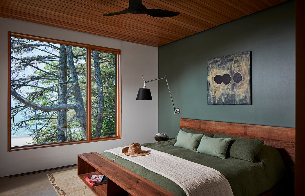 Cozy cabin bedroom with wood-paneled ceiling, large window, and rustic furniture.