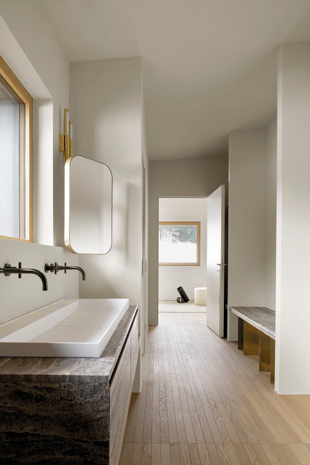 A minimalist bathroom with a large vanity, oval mirror, and wooden flooring leading to an adjoining room.