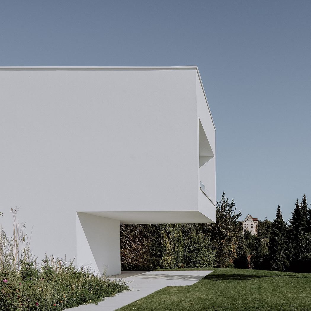 A modern white structure with clean lines and a minimalist design, set against a forested backdrop.