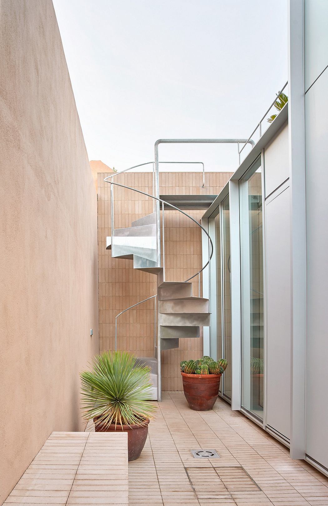 A modern outdoor staircase leads to a balcony with potted plants and glass doors.