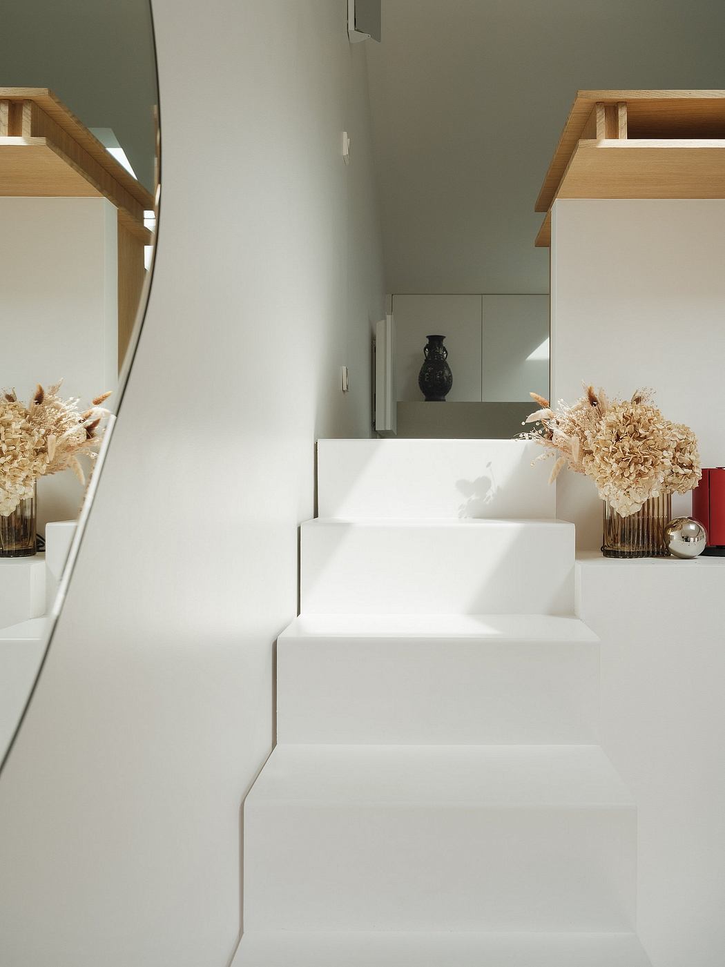 Minimalist white staircase with wooden shelves and decorative vases.