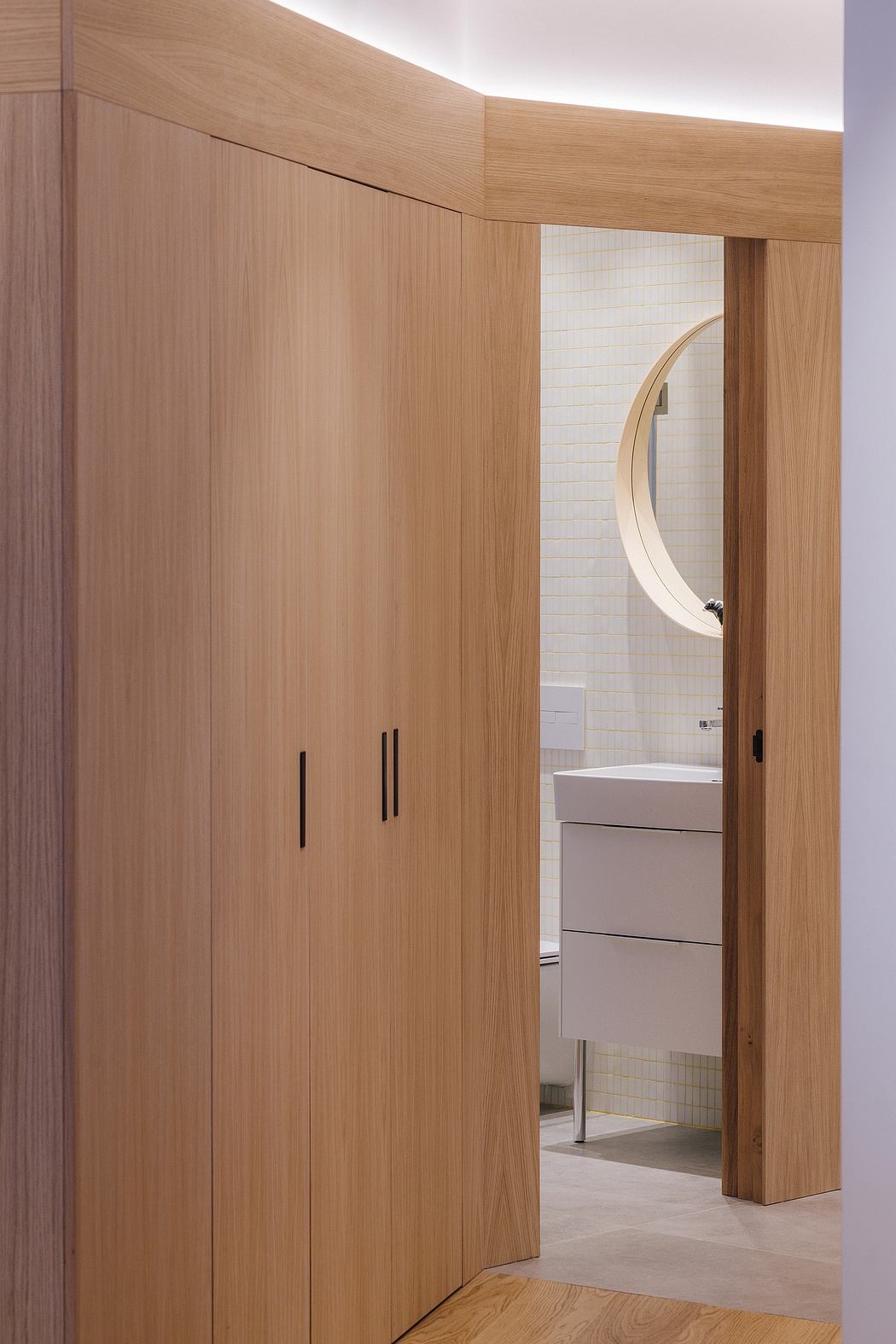 Curved wooden walls and a round mirror frame define this minimalist bathroom space.