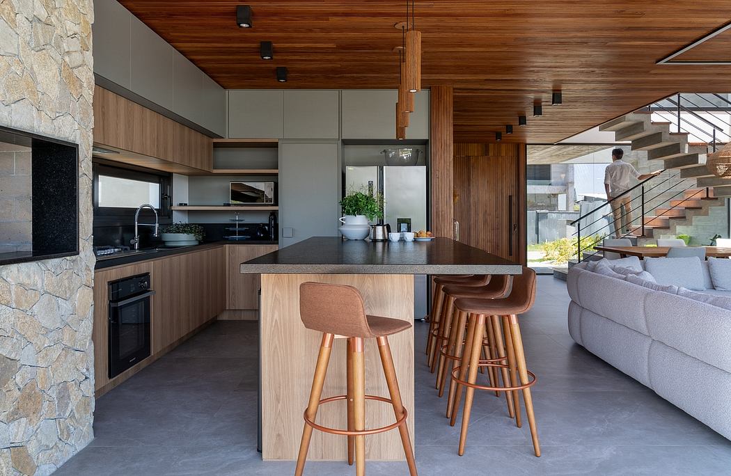 Sleek, modern kitchen with wooden accents, stone wall, and elevated staircase. Chic, functional design.