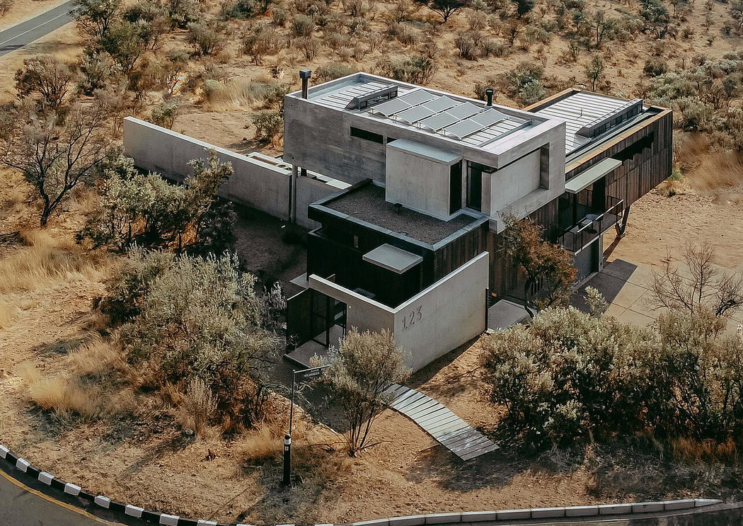 A striking desert home with angular concrete forms, solar panels, and a wooden walkway.