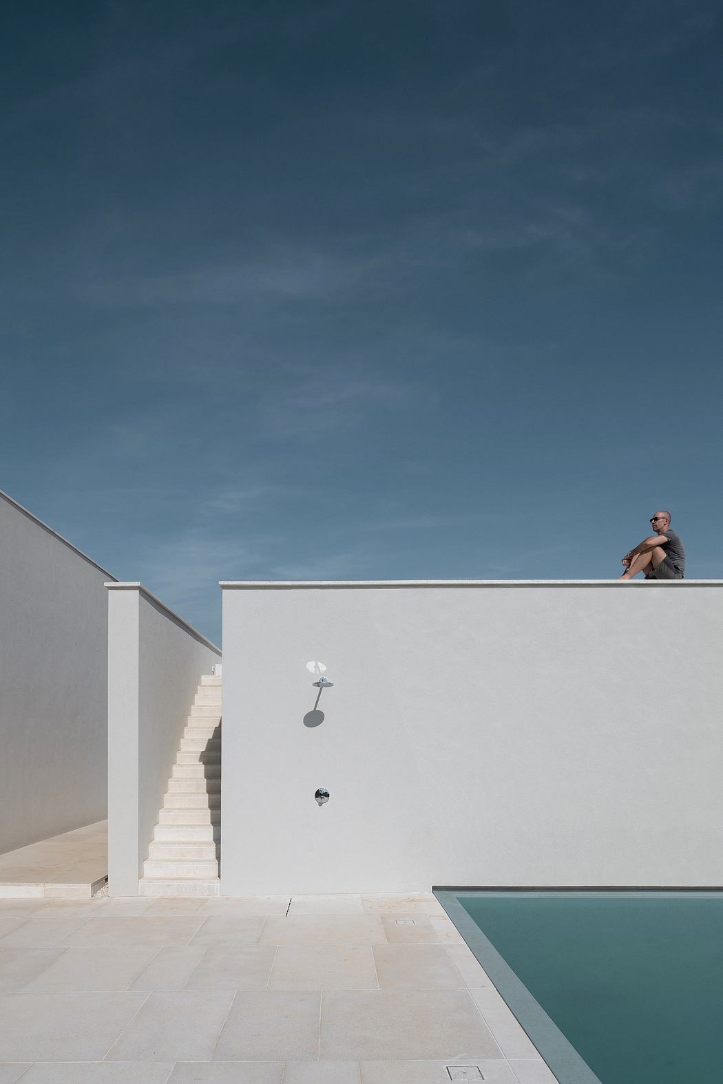 Minimalist exterior with clean lines, recessed lighting, and a swimming pool against a stark, blue sky.