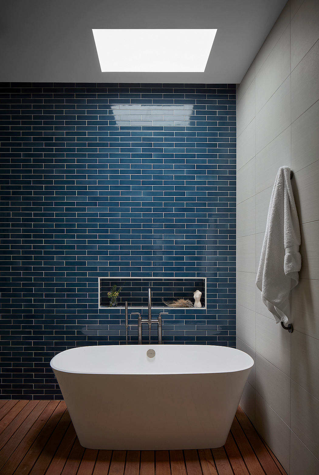 Minimalist bathroom with freestanding tub, blue tile wall, and wooden floor.