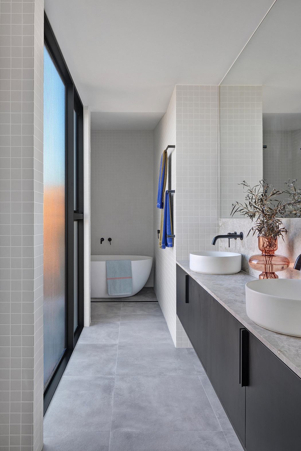 Modern, minimalist bathroom with gray tiles, vessel sinks, and a black-framed window.