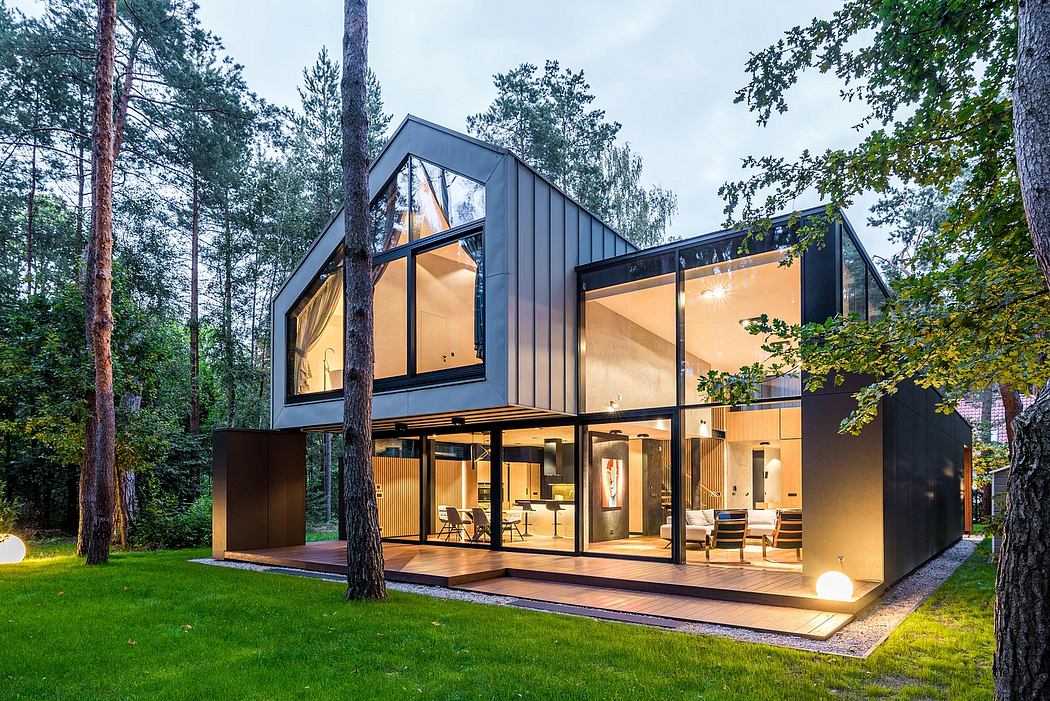 A modern, two-story home with large glass windows overlooking a lush forest. Sleek, angular architecture accentuated by natural materials.