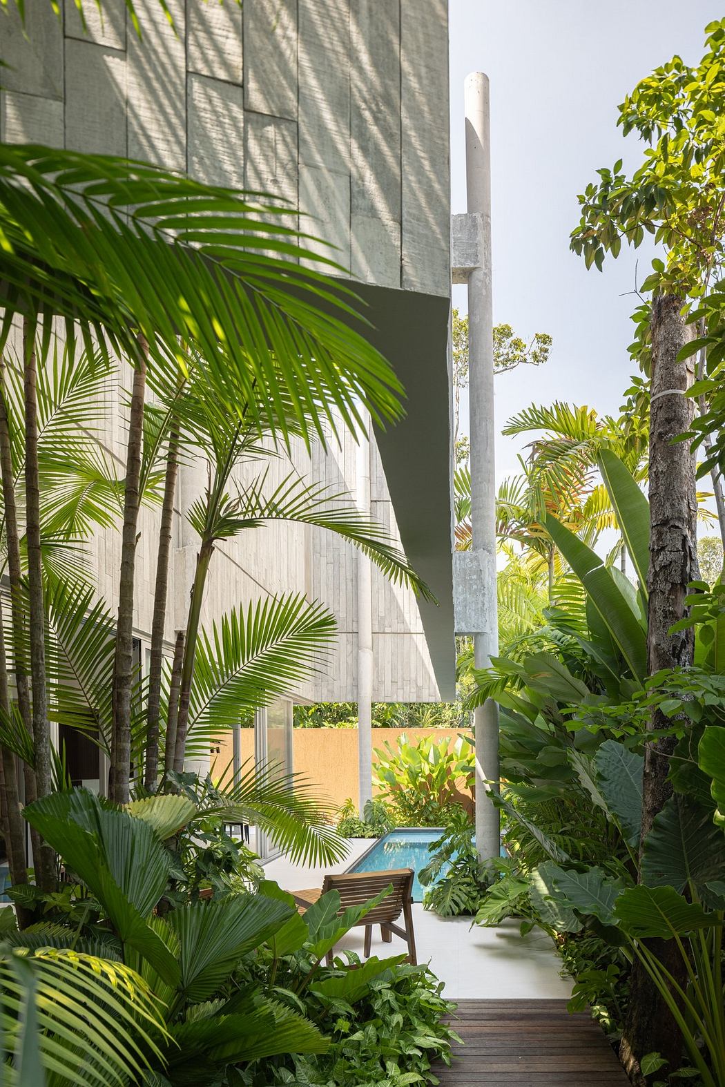 Lush tropical landscape surrounds a modern, concrete structure with a pool and wooden deck.