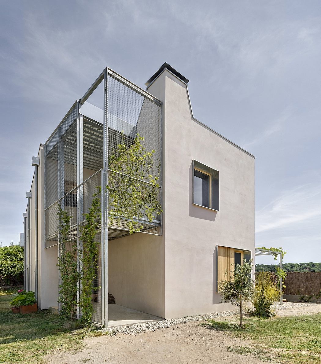 Angular modern concrete house with metallic grid facade, gravel path, and greenery.