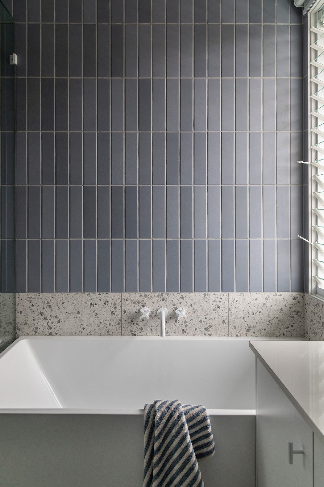 Sleek bathroom with gray tiled walls, white bathtub, and striped towel.