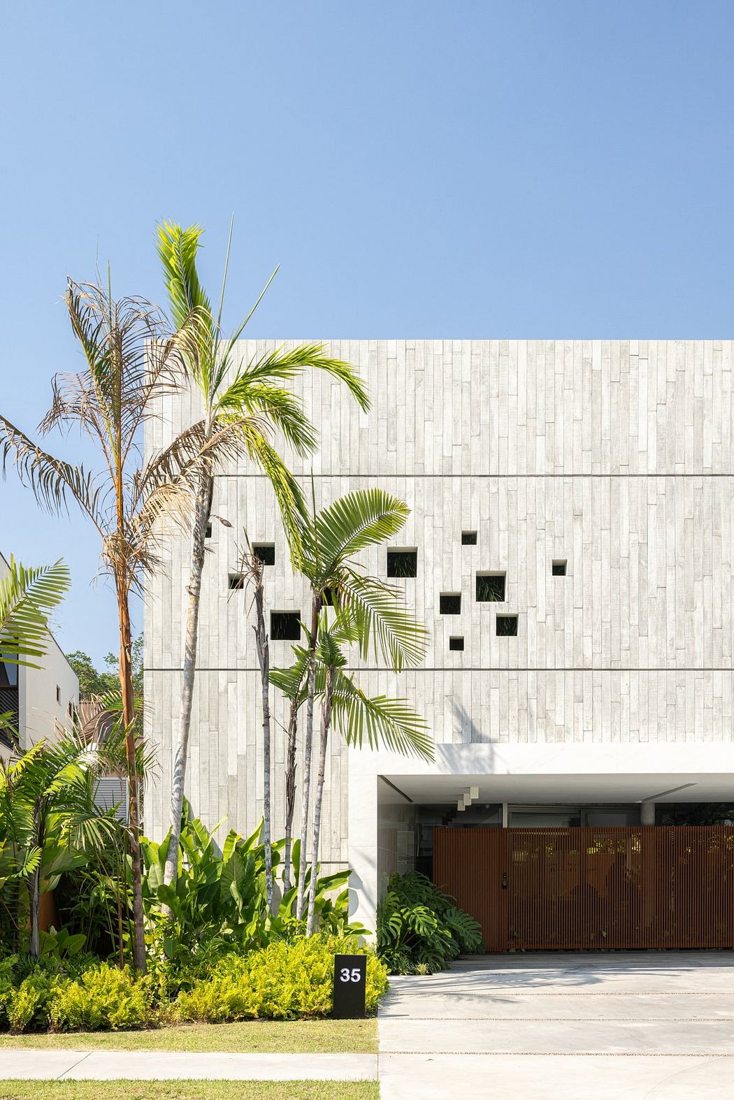 A modern white building with tropical landscaping, featuring palm trees and lush foliage.
