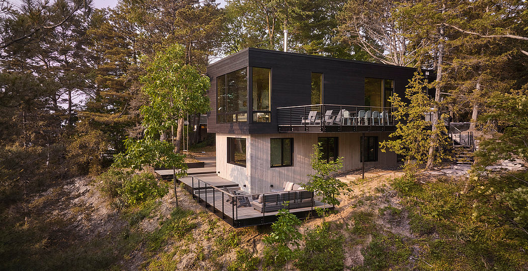 A modern two-story cabin surrounded by lush greenery, with large windows and a balcony.