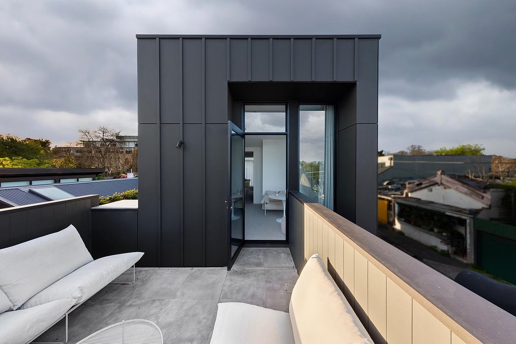 The image depicts a modern building with a sleek, minimalist exterior featuring large windows and a covered balcony area.