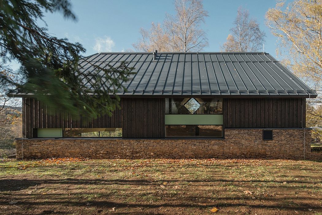 A modern, wooden cabin with a metal roof and stone foundation, surrounded by fall foliage.