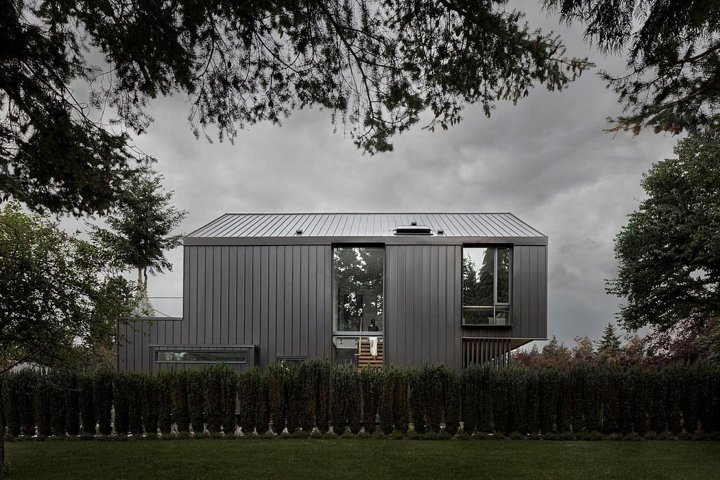 A modern, dark-colored, angular residential building nestled among trees.