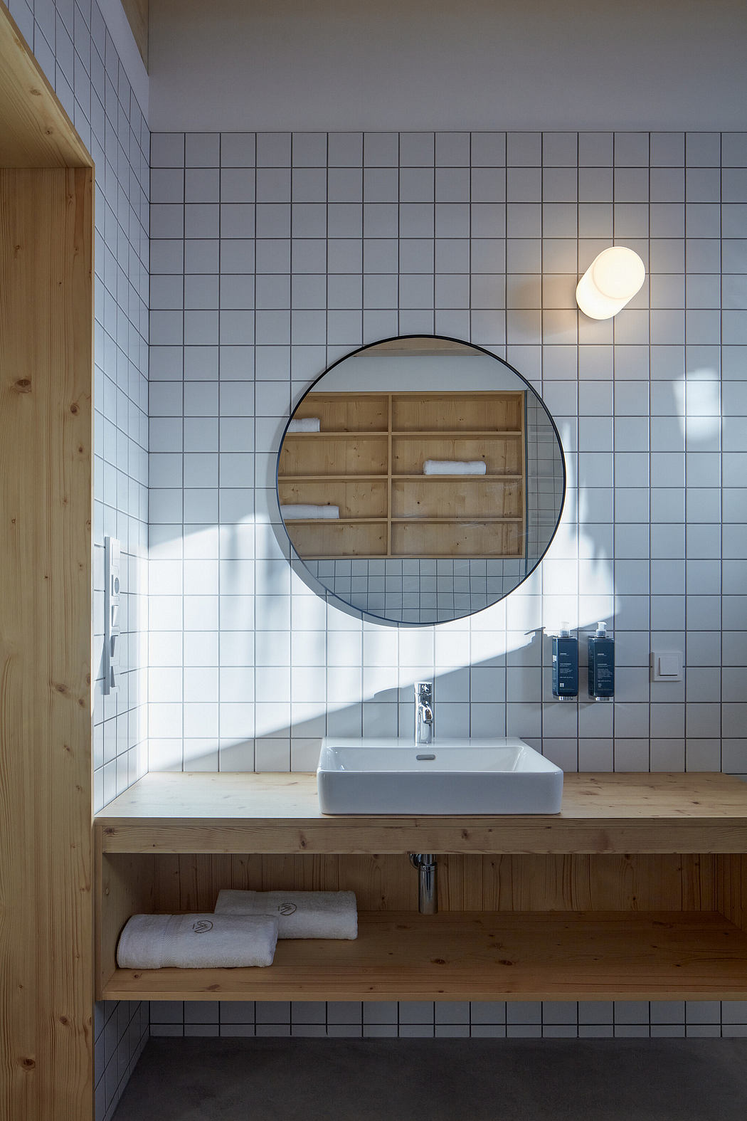A modern bathroom with a round mirror, tiled walls, and a wooden vanity counter.