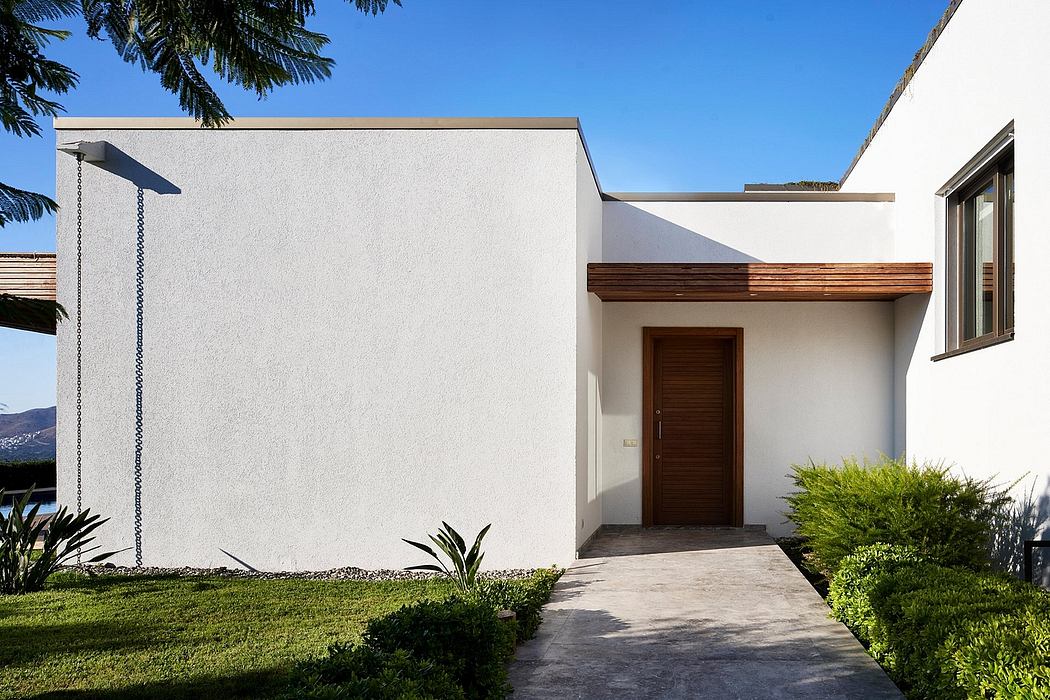 A modern, minimalist exterior with a wooden roof overhang and a paved walkway leading to the entrance.